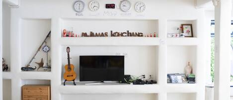 Una sala de estar con televisor, cajones de madera, una guitarra y un reloj de pared que muestra múltiples zonas horarias.