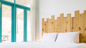 Una cama con sábanas blancas en una habitación con cabecera de madera, ventanas grandes y vistas al exterior.