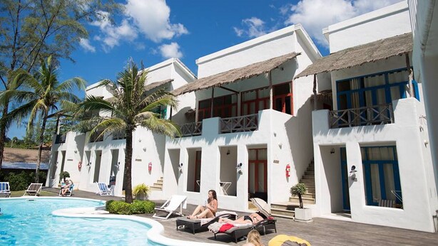 Un resort con piscina, sillas de descanso y un edificio de dos pisos con techo de paja.