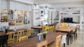 Un comedor moderno con mesas y sillas de madera, lámparas colgantes y una cocina al fondo.