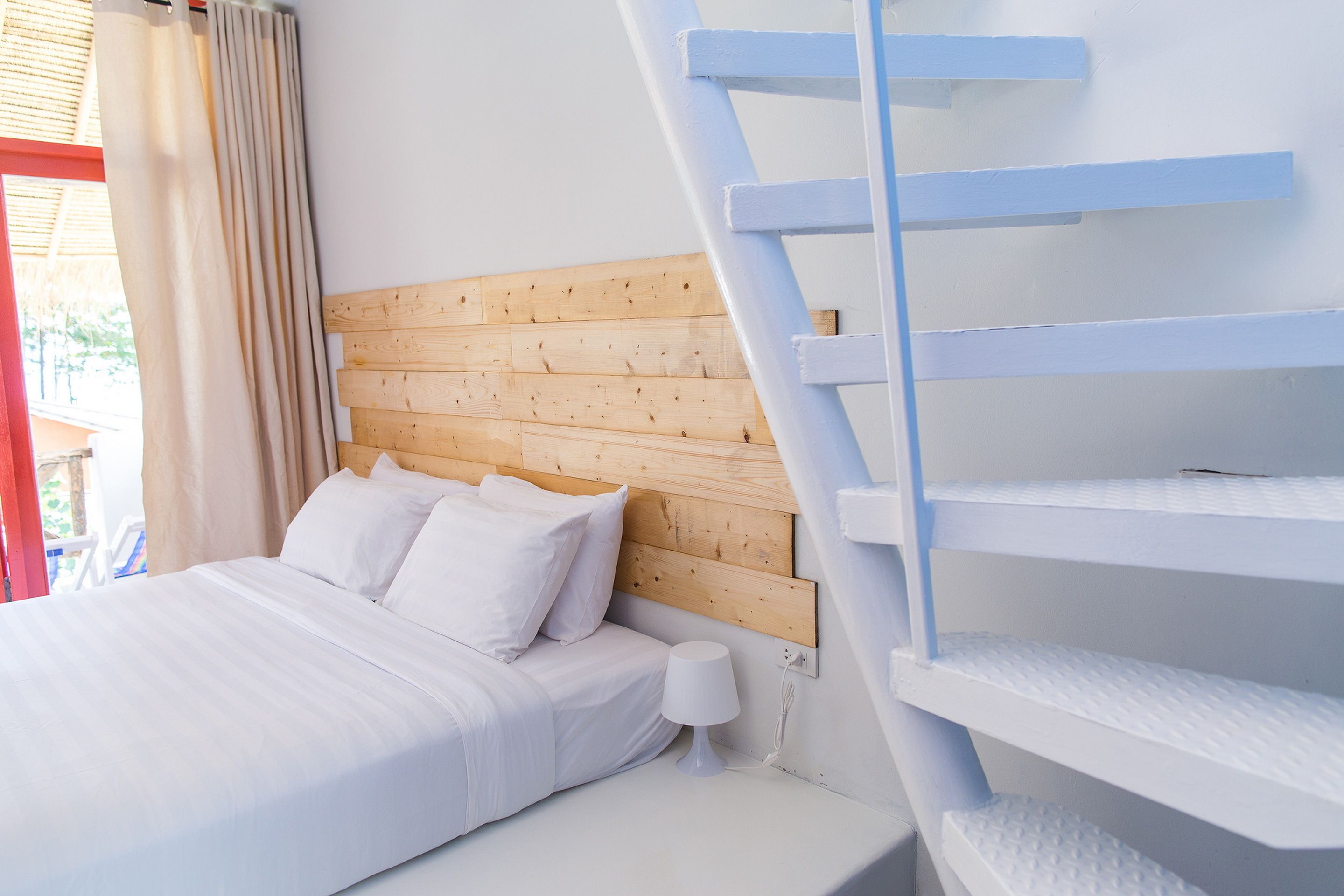 A bedroom with a wooden headboard, a bed with white bedding, a bedside lamp, and a white staircase.