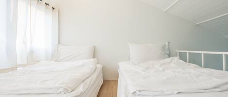 Habitación doble con dos camas, ropa de cama blanca y suelo de madera.
