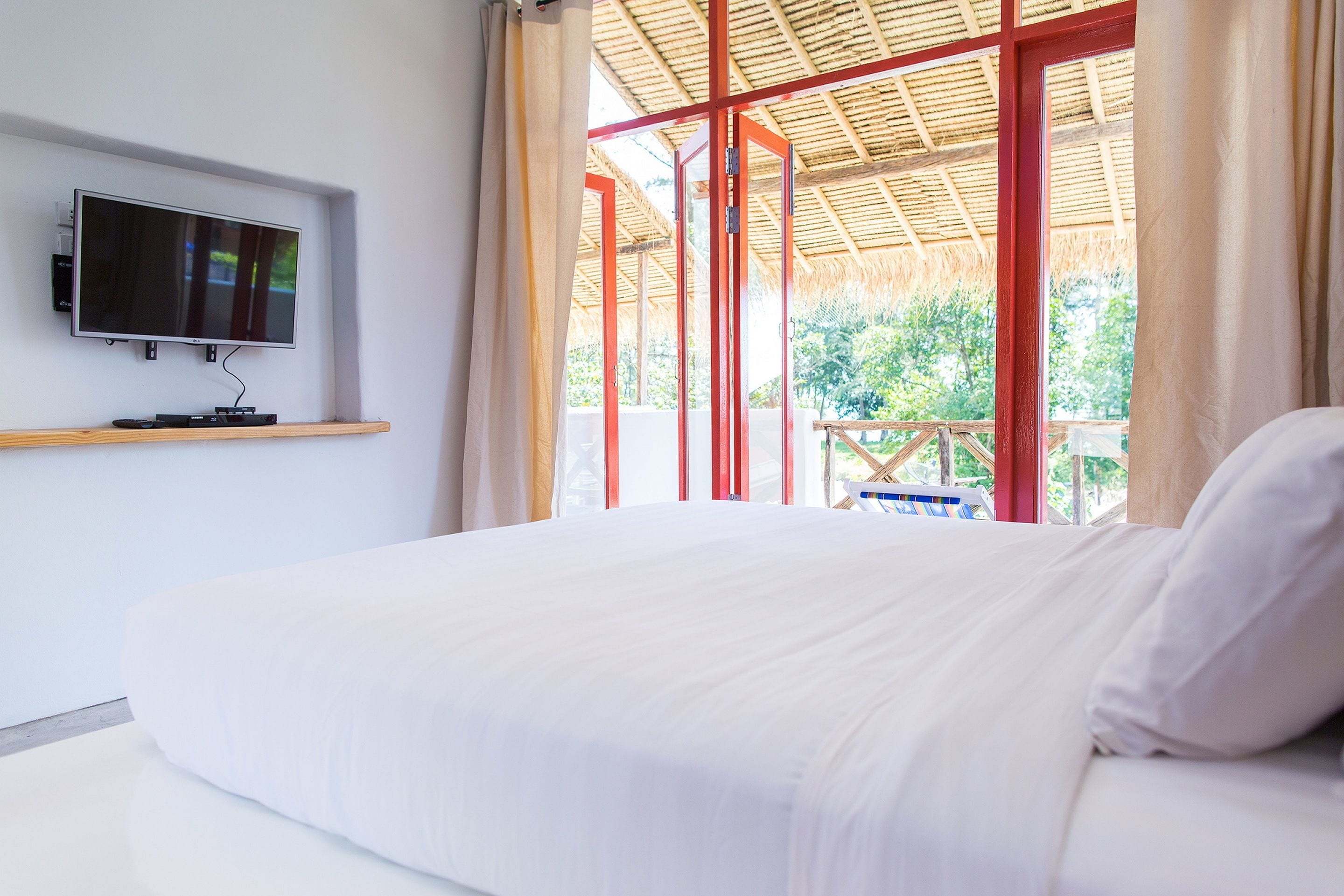 A bedroom with a bed, a TV mounted on the wall, and a view of the outdoors through large windows.