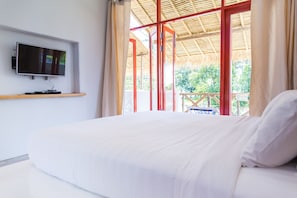 A bedroom with a bed, a TV mounted on the wall, and a view of the outdoors through large windows. - Pajamas Koh Chang (Ko Chang)