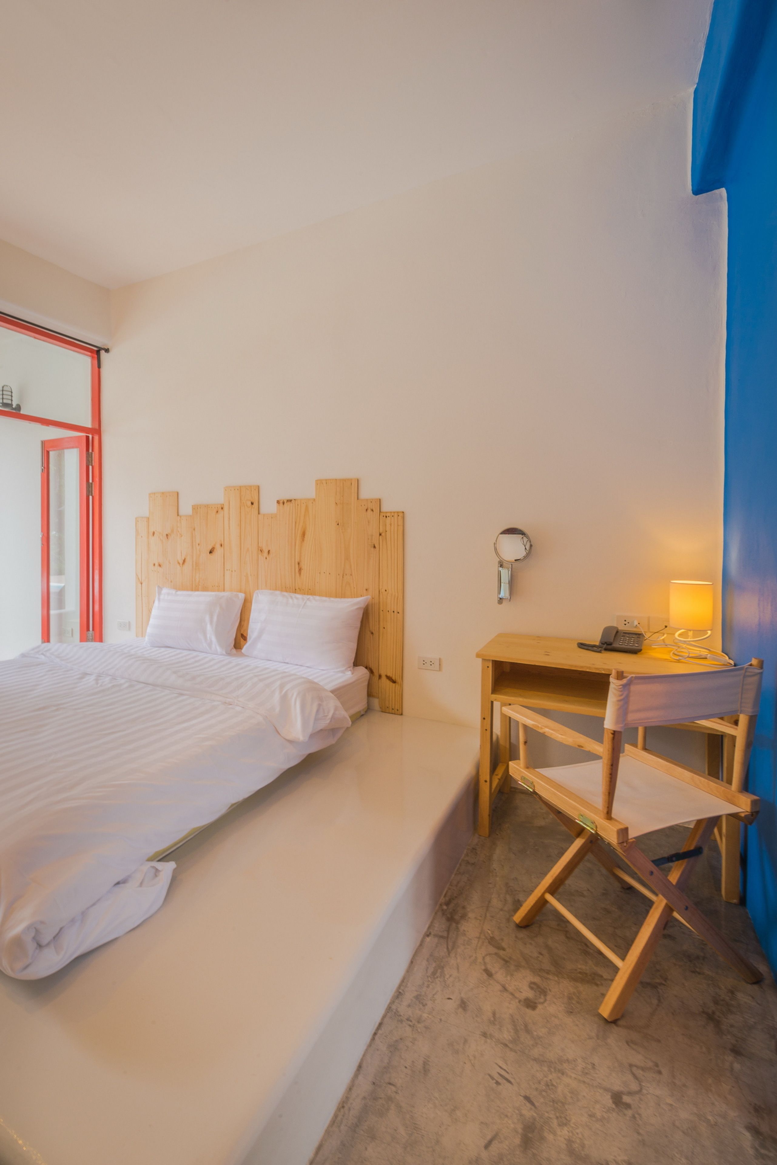A bedroom with a wooden headboard, a bed with white linens, a bedside table with a lamp, and a chair.