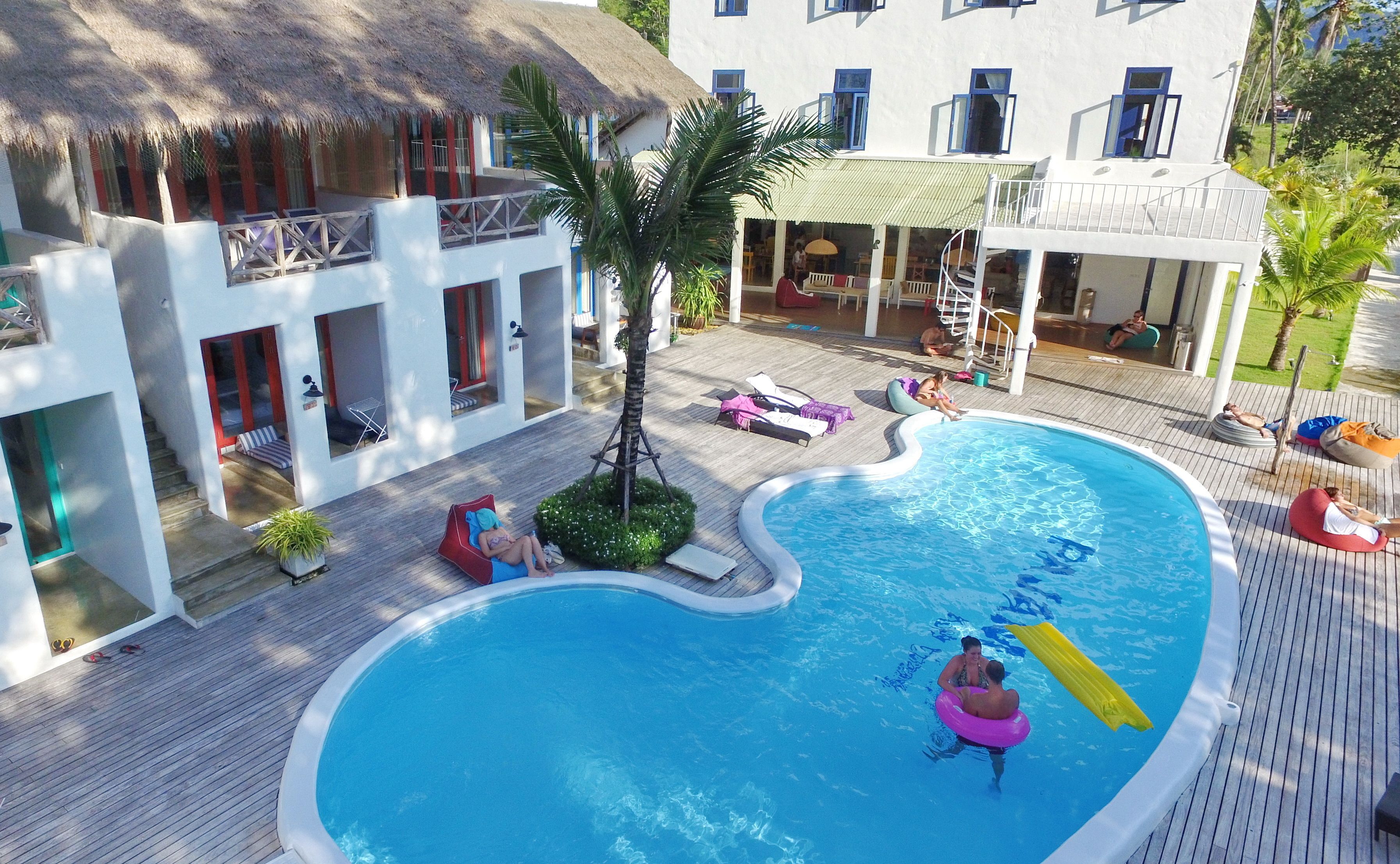 Un resort con piscina, sillas de descanso y un edificio con techo de paja.