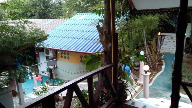 Une vue depuis un balcon donnant sur une piscine, un petit bâtiment avec un toit bleu et la verdure environnante.