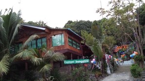 Un bungalow à l’extérieur en bois, une enseigne indiquant « Bungalow Comong » et un escalier menant à l’entrée.