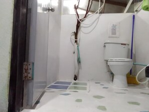 A small bathroom with a toilet, a shower area, and a door with a metal handle.