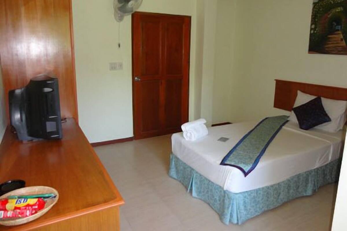 Een hotelkamer met een houten bureau, een bed met een blauwe sprei, een witte handdoek en een schilderij aan de muur.