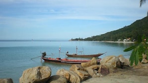 A calm coastal scene with two boats docked near rocks and a clear view of the sea. - VIVA on the Beach Hotel (Ko Pha-ngan)