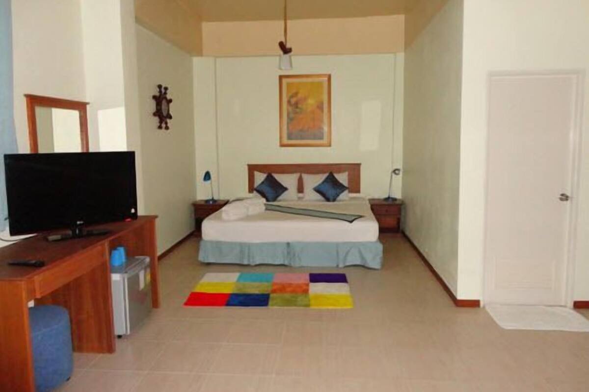 Een hotelkamer met een bed, een bureau met een televisie, een kleurrijk vloerkleed en een deur.
