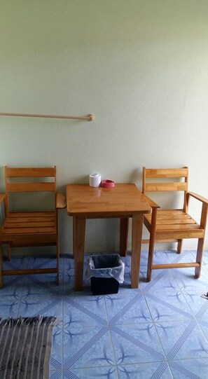 A small room with a wooden table and two chairs, a trash bin, and a wall-mounted towel rack.