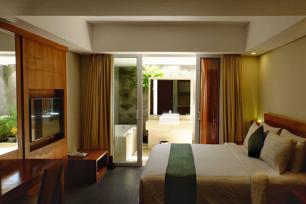 A hotel room with a bed, a TV, a desk, and a bathroom visible through an open door.