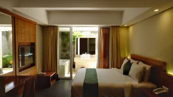 Quarto de hotel com uma cama, televisão, escrivaninha e banheiro visível através de uma porta aberta.