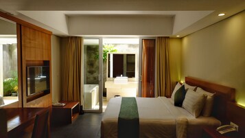 Quarto de hotel com uma cama, televisão, escrivaninha e banheiro visível através de uma porta aberta.