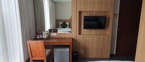 A hotel room with two beds, a desk, a television, and a small kitchenette.