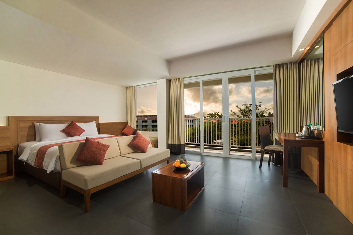 A hotel room with a bed, sofa, coffee table, TV, and a balcony with a view.