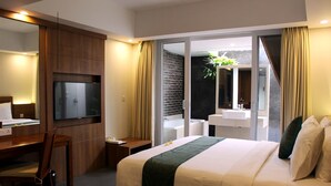 A hotel room with a bed, a desk, a television, a bathroom with a sink and mirror, and a sliding glass door to the outside. - Paragon Hotel Seminyak (Keroboken Kelod)