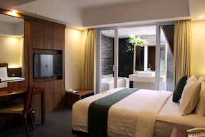 A hotel room with a bed, a desk, a television, a bathroom with a sink and mirror, and a sliding glass door to the outside. - Paragon Hotel Seminyak (Keroboken Kelod)