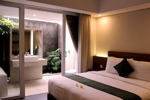 A hotel room with a bed, a bathroom with a sink, and a sliding glass door leading to an outdoor area. - Paragon Hotel Seminyak (Keroboken Kelod)