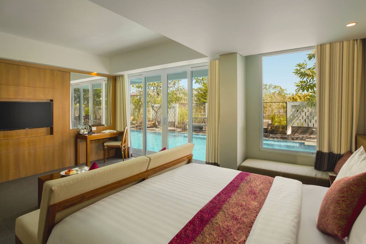 A hotel room with a large bed, a desk with a chair, a TV, and a view of a swimming pool.