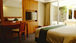 A hotel room with a bed, a desk, a chair, a TV, a bathroom with a sink, and a view of the outside. - Paragon Hotel Seminyak (Keroboken Kelod)