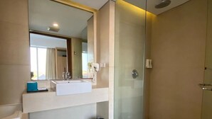 A modern bathroom with a glass shower enclosure, a large mirror, and a white towel on the floor. - Paragon Hotel Seminyak (Keroboken Kelod)