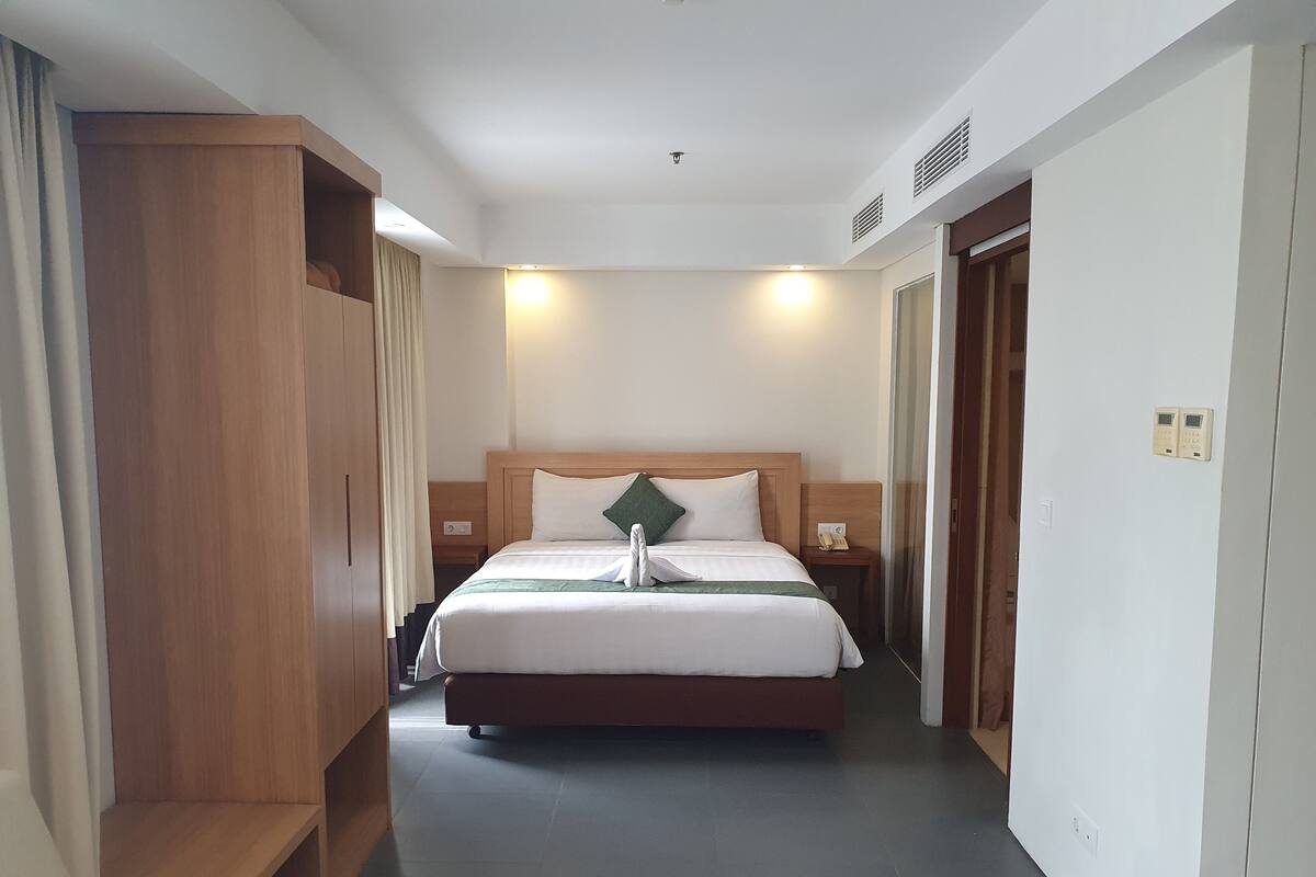 A hotel room with a bed, bedside tables, a wooden wardrobe, and a door.