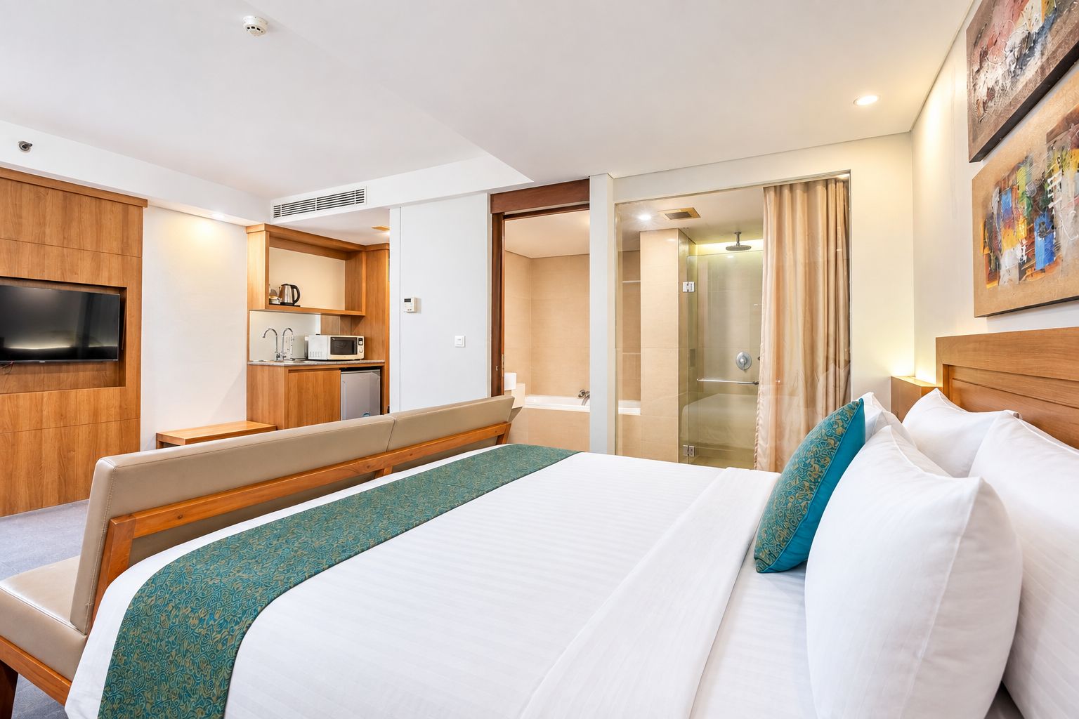 A hotel room with a bed, a seating area, a kitchenette, a shower, and a television.
