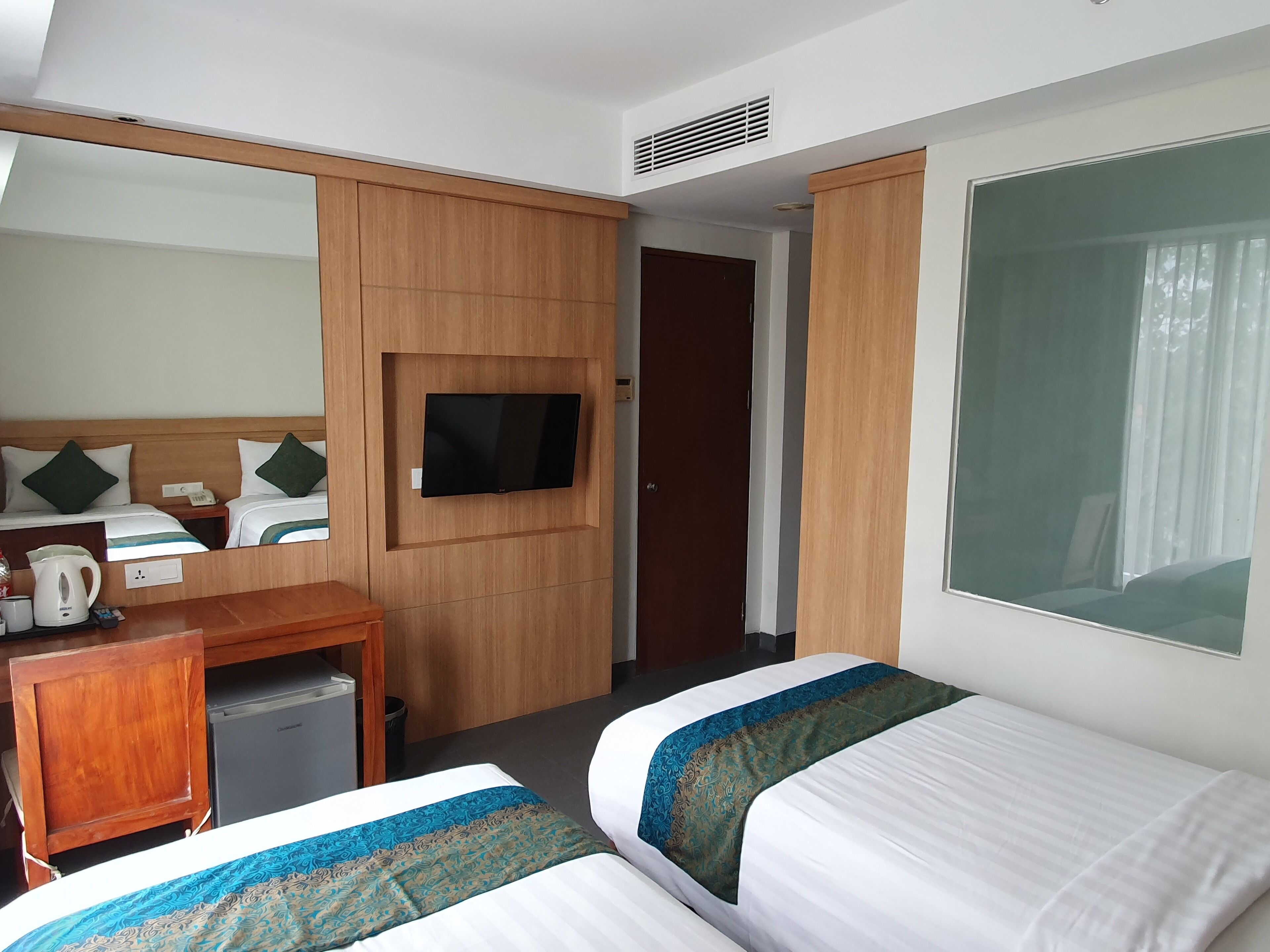 A hotel room with two beds, a TV, a desk with a kettle, and a small fridge.