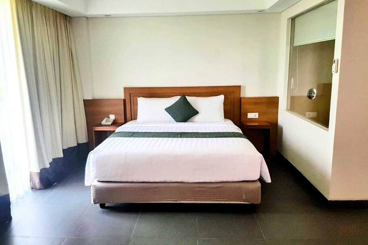 A hotel room with a large bed, a nightstand, a telephone, and a window with curtains.