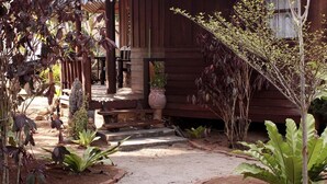 A wooden house with a porch, steps leading to the entrance, and a garden with various plants. - Dancing Elephant Beach Club - Hostel (Ko Pha-ngan)
