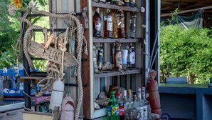 A rustic outdoor bar area with shelves stocked with various bottles, a wooden sign with 'FUN' written on it, and a rope decoration. - Dancing Elephant Beach Club - Hostel (Ko Pha-ngan)