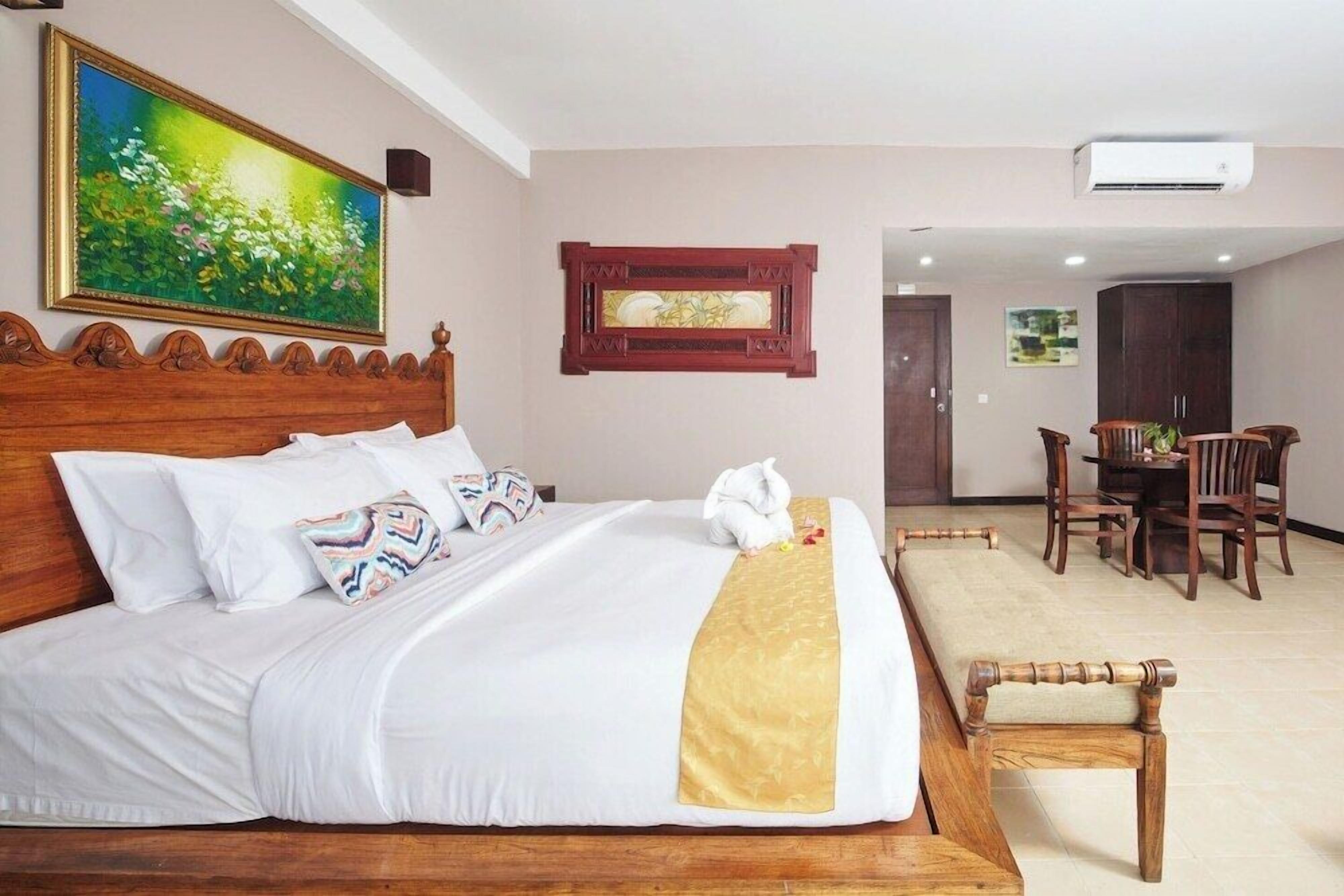 Een hotelkamer met een houten bed, een zithoek met stoelen en een schilderij aan de muur.