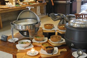 A buffet setup with various dishes and a large pot of rice. - Grand Santhi Hotel (Denpasar)
