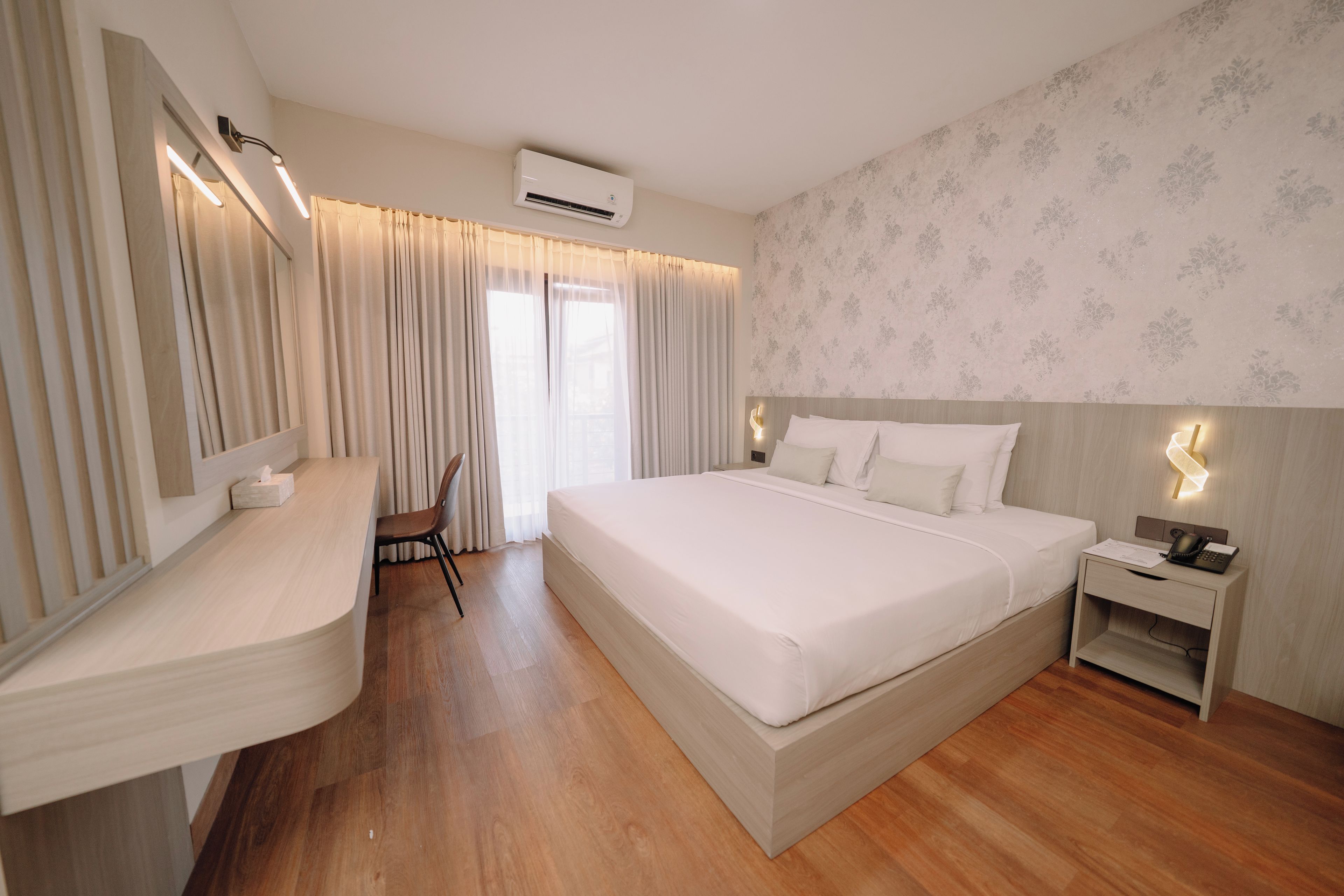 Een hotelkamer met een groot bed, nachtkastje, stoel en een airconditioning.