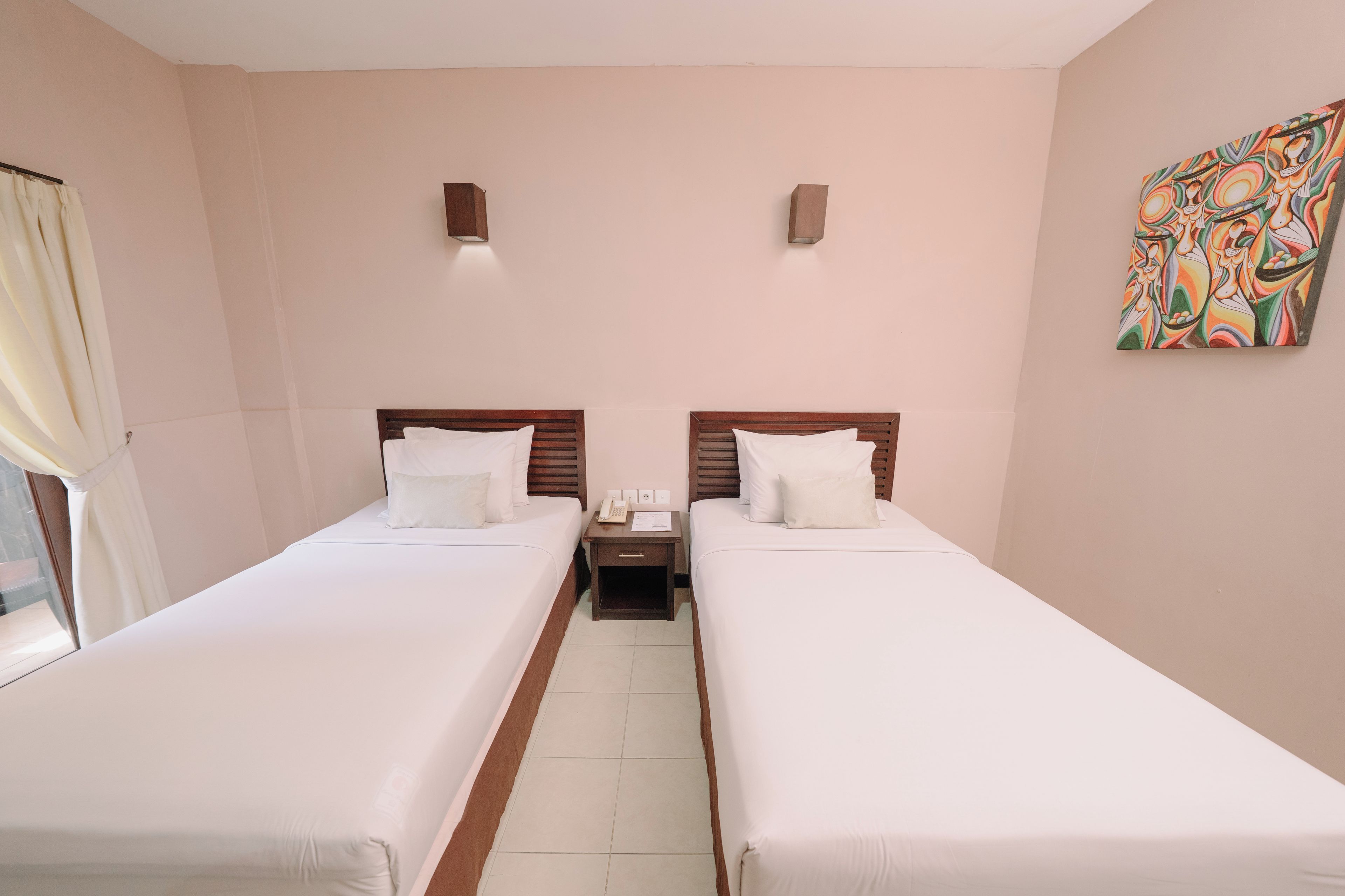 A hotel room with two single beds, a nightstand with a phone and papers, a window with curtains, and a colorful abstract painting on the wall.