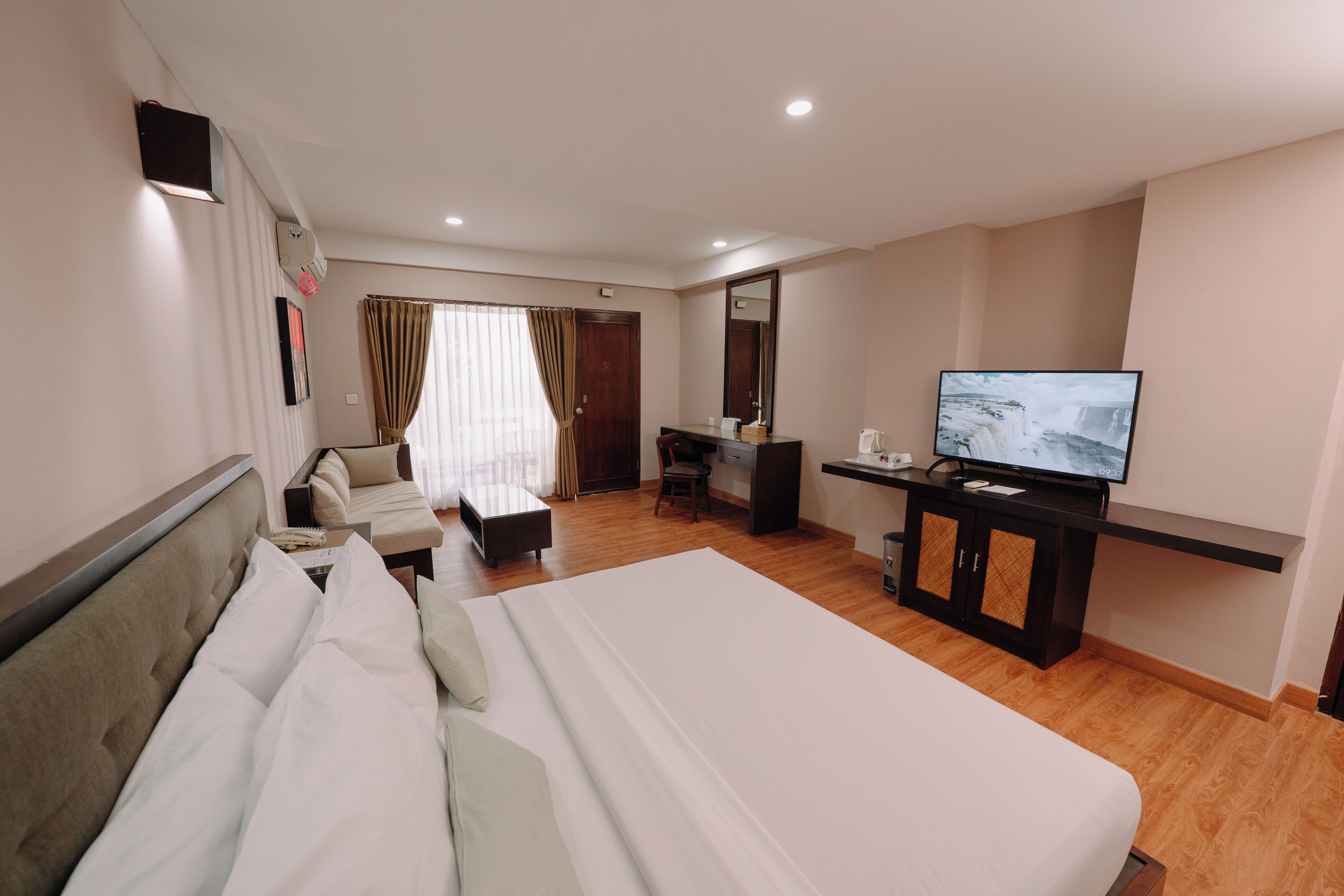 A hotel room with a bed, a desk, a television, and a view of a waterfall.