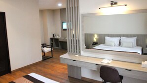 A modern hotel room with a large bed, a desk, a chair, a mirror, and a television. - Grand Santhi Hotel (Denpasar)