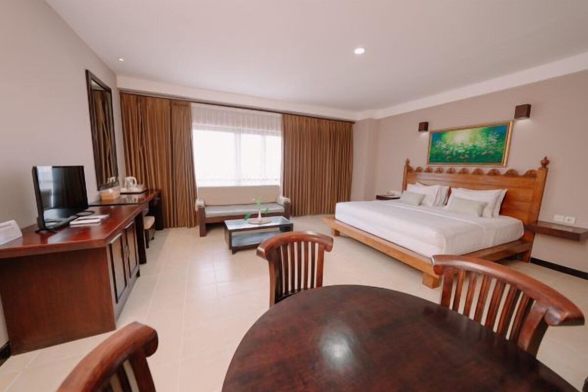 A hotel room with a bed, a desk with a TV, a dining table, and a window with curtains.