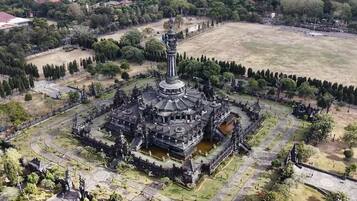 An aerial view of a large, historic temple complex with multiple structures, including a central tower, surrounded by pathways and greenery.
