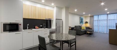 A modern kitchen with white cabinets, a dining table with chairs, a sofa, and a large window with curtains.