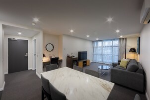 Uma sala de estar moderna com área de jantar, sofás cinzas, uma TV e um ar condicionado instalado no teto.