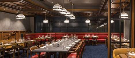 Un restaurante con mesas largas, cabinas acolchadas rojas e iluminación colgante.