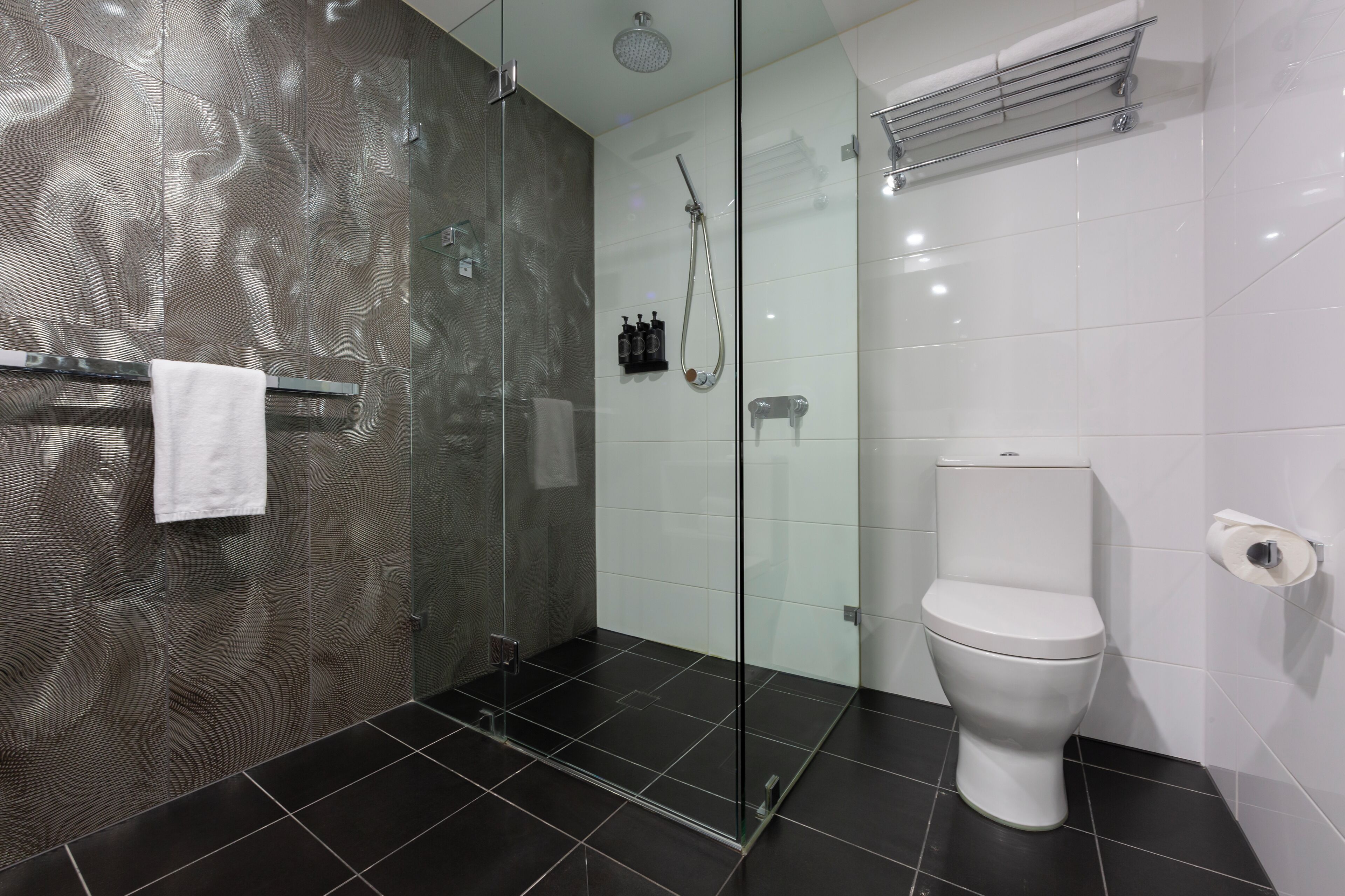 A modern bathroom with a glass shower enclosure, a white toilet, and a towel rack.