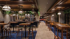 A bar area with wooden tables and stools, a counter with a barista, and hanging plants. - Avenue Hotel Canberra (Braddon)