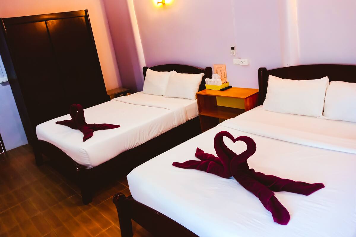 Two twin beds with white linens and heart-shaped towels, a bedside table with a lamp, and a wall-mounted light fixture.