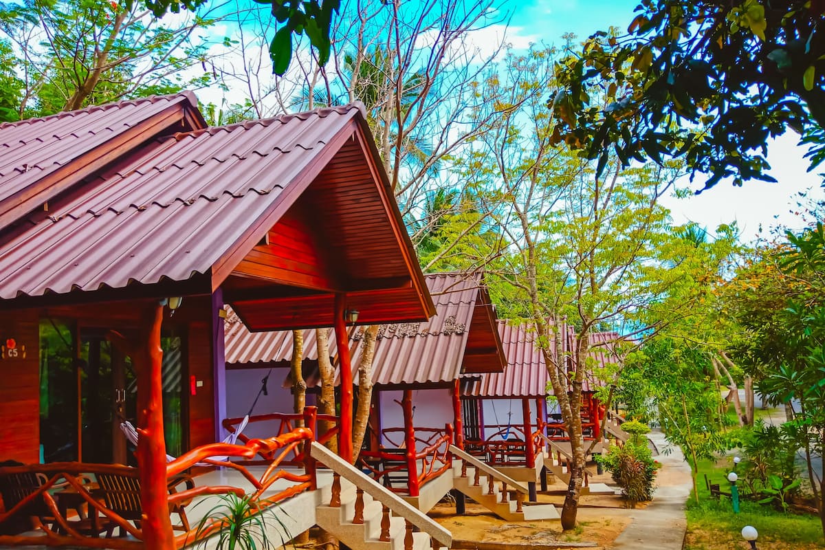 A row of wooden cabins with red roofs, each with a porch and a staircase leading to the entrance.