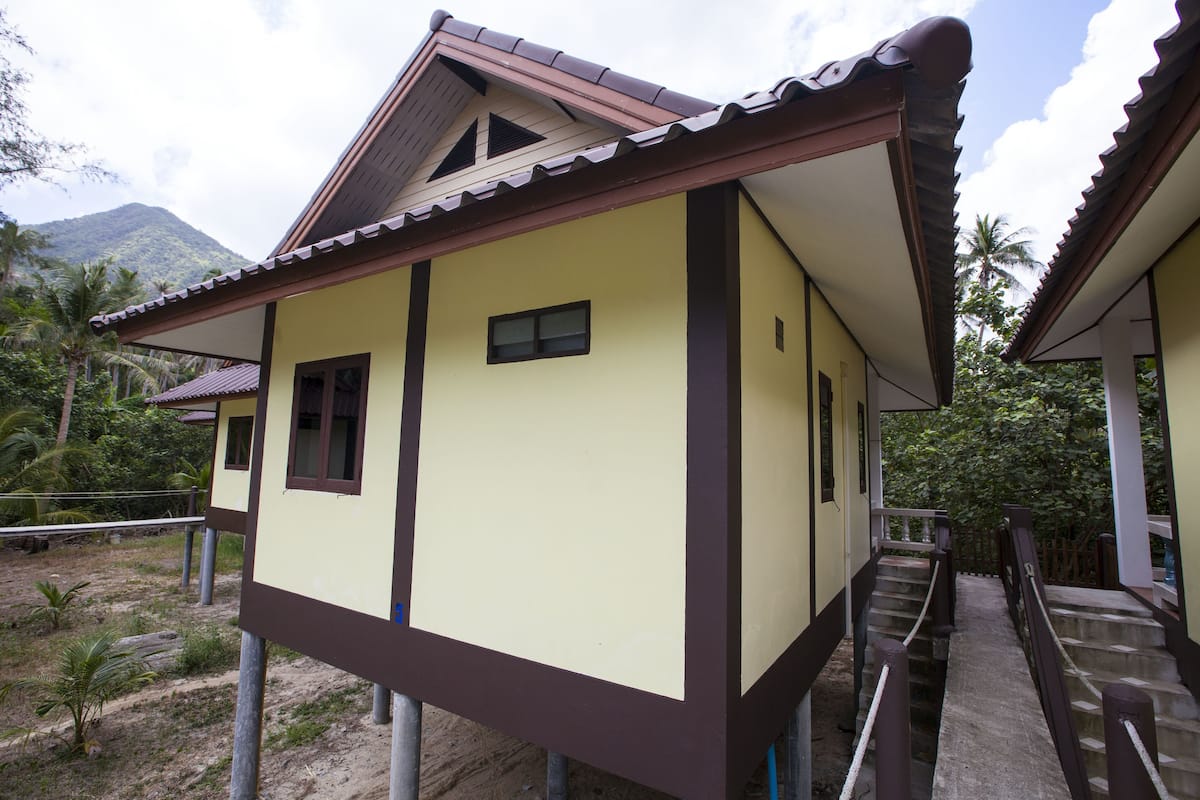 A two-story building with a brown roof and beige walls, featuring a staircase and a small window.